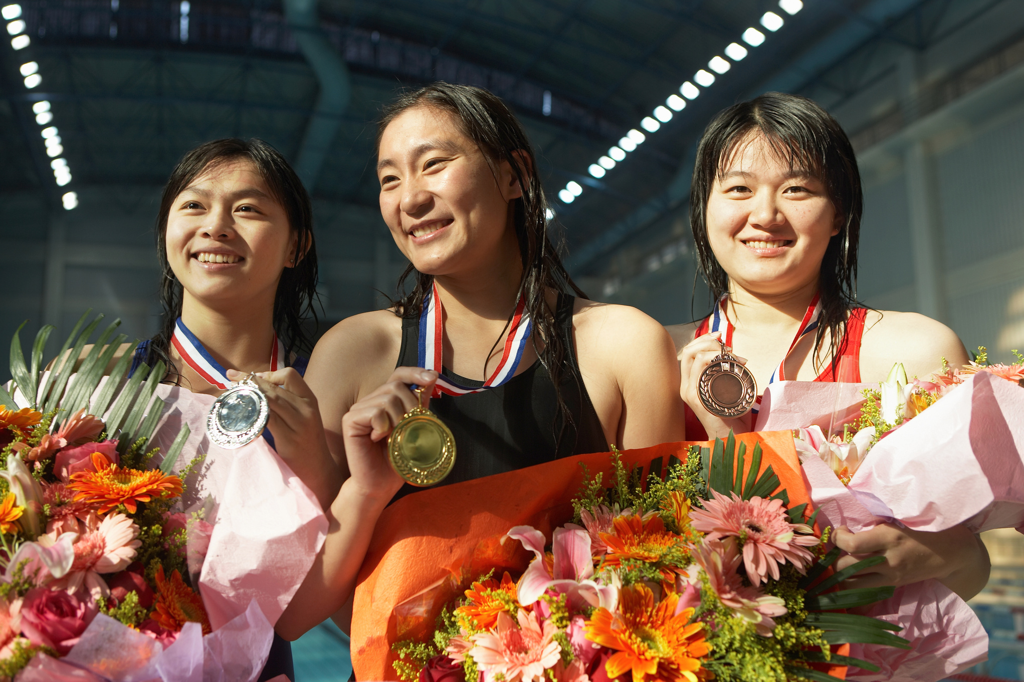 Three young female swimmers displaying medals, smiling